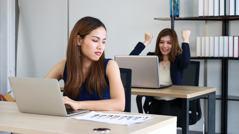 Woman looking annoyed at happy colleague