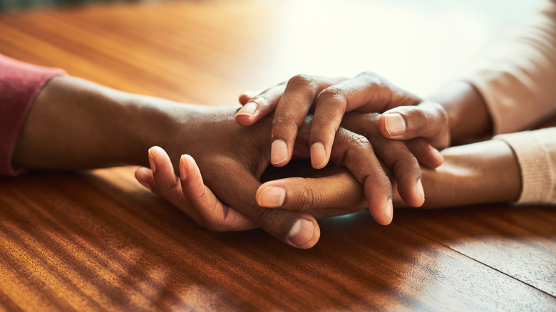 A woman's hands hold a man's hand compassionately