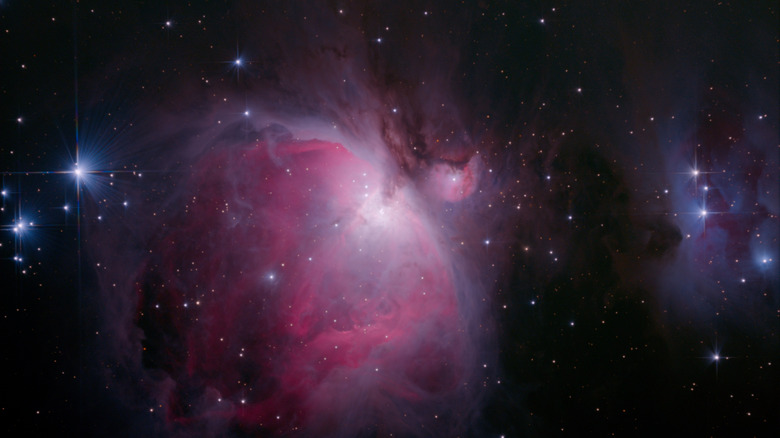 A pink-purple cloud of gases and diamond-like stars in the night sky