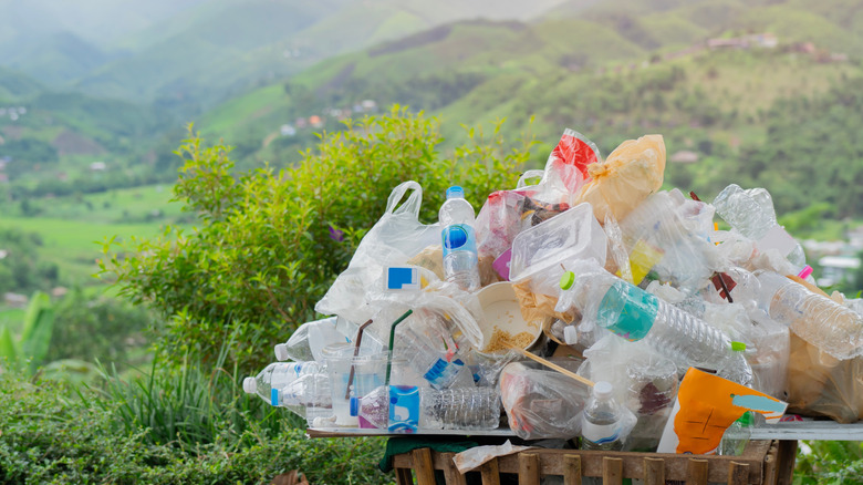 Dozen of empty plastic bottles and containers overflow from a wooden trash bin