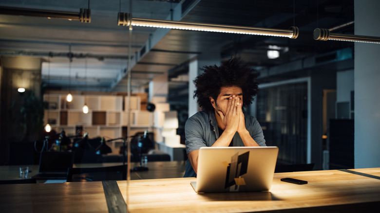 A person sits in front of a laptop holding their hands to their face with an exasperated expression