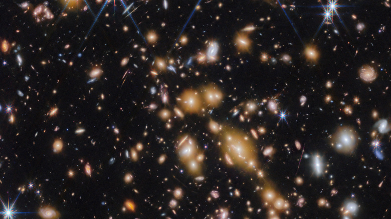 A cluster of countless galaxies and stars shine brilliantly against the dark background of space