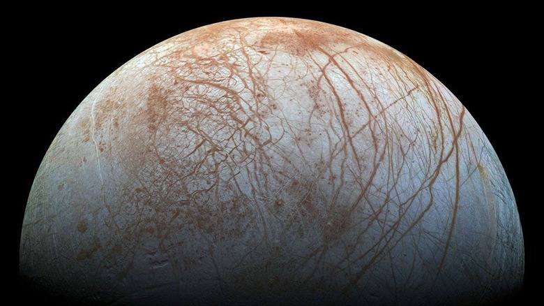 The pale blue sphere of Europa against a black backdrop with light brown cracks winding jaggedly across its surface