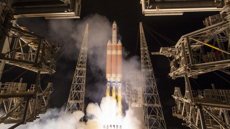 A rocket carrying the Parker Solar Probe launches from its pad surrounded by several metal apparatuses