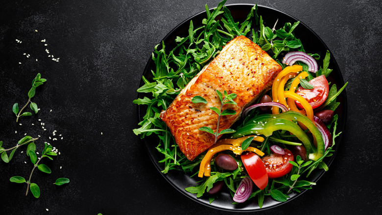 A plate of salmon, peppers, arugula, and red onions