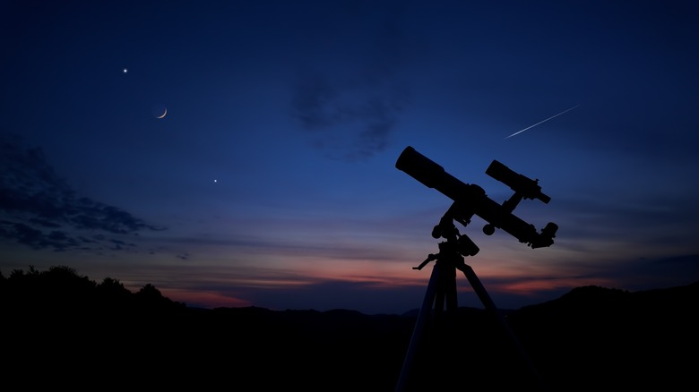 A telescope is silhouetted against a starry sky at dusk