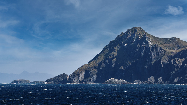 A jagged rocky hill with a wild wavy ocean in the foreground