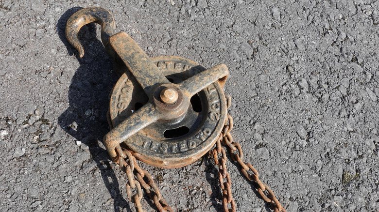 Rusty antique block and tackle sitting on asphalt