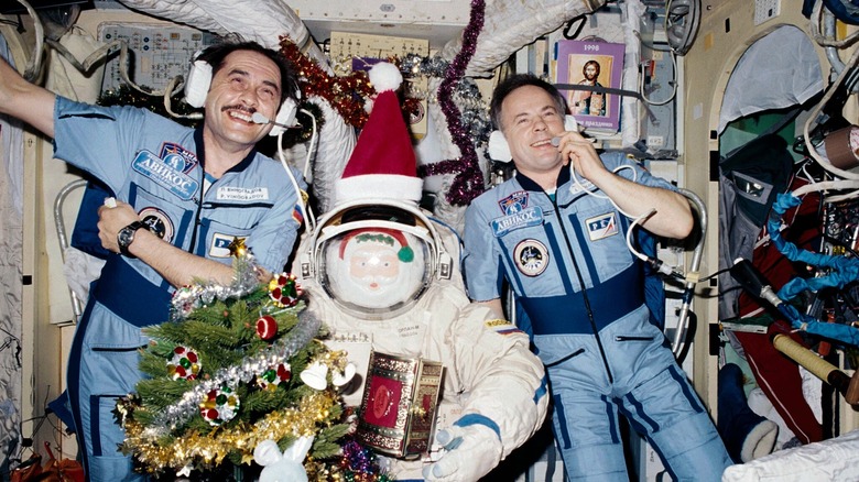 Two astronauts pose behind a Santa Claus figure in a space suit aboard a space shuttle