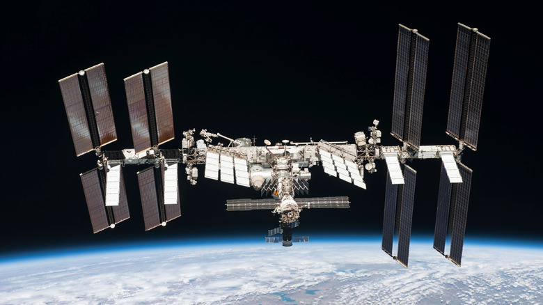 The International Space Station in orbit above the curvature of the Earth, with solar panels and dozens of other arrays linking the station together