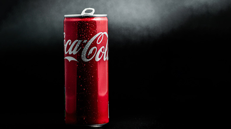 A red Coca Cola can covered in drops of condensation against a black backdrop