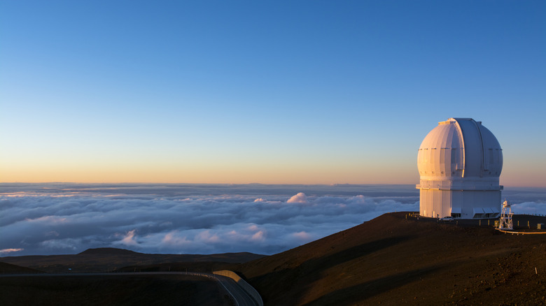 A white dome on a hill above the clouds at sunset with a clear cerulean blue sky above