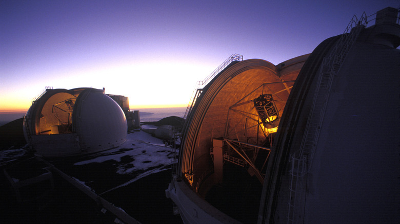 The dimly-lit open domes of the telescopes at Keck Observatory at dusk with a purple sky above