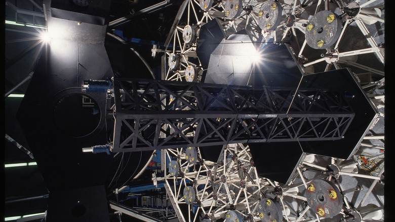 An image of the complex machinery of the inside of an observatory's telescope lens featuring glassy hexagonal patterns amidst white triangular metal trusses