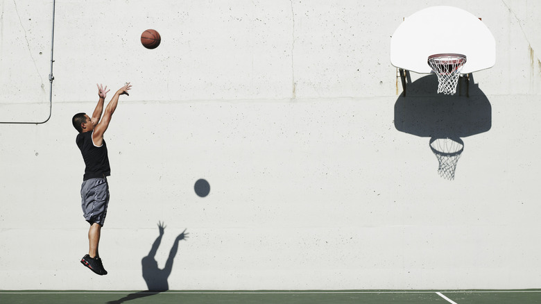 Man shooting ball at outdoor basketball hoop