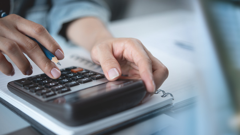 Close up of hands typing on calculator