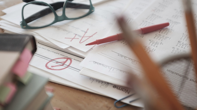 Stack of graded tests with a red pen and glasses