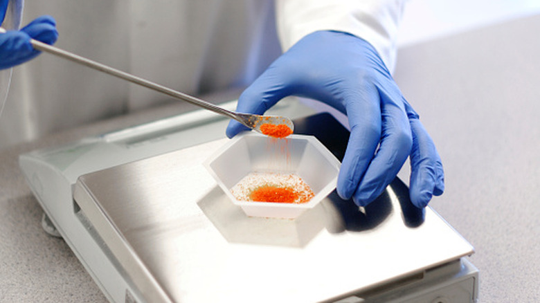 Scientist measuring out crystalline orange solid onto a scale