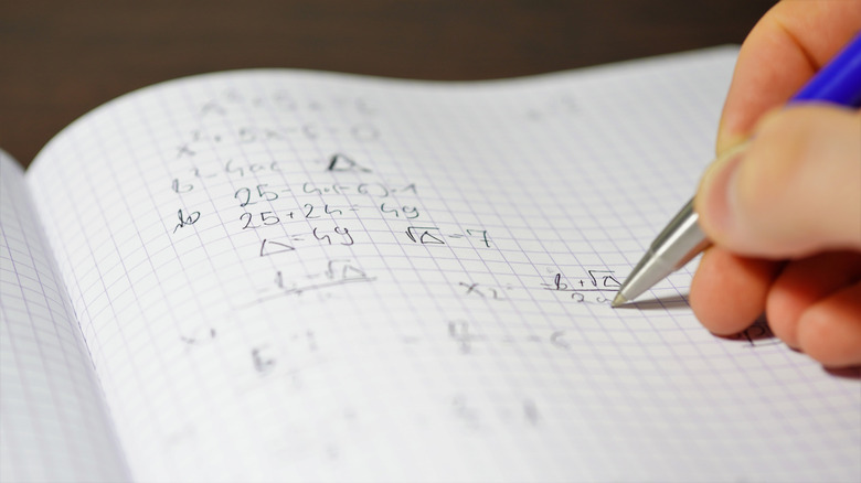 Hand holding pen over page with quadratic equations