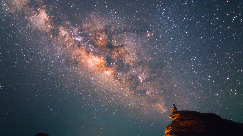 A person on a rocky ledge looking up at the stars at night