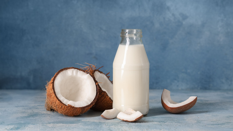 Coconut milk in a bottle with coconuts in the background