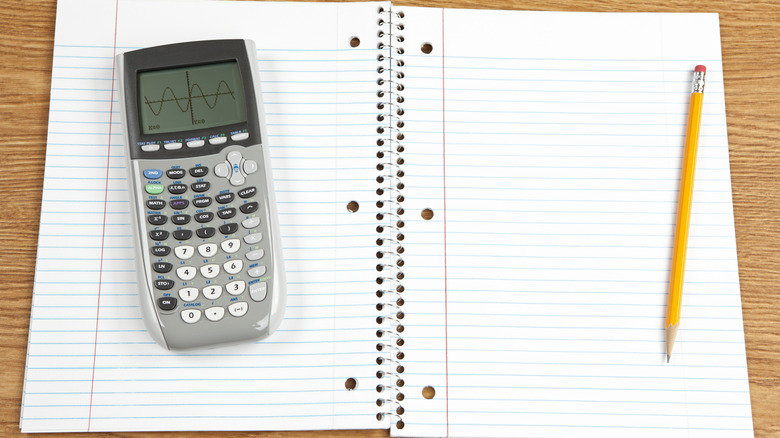 Ti-84 graphing calculator on the left side of an open school notebook with a pencil on the right side