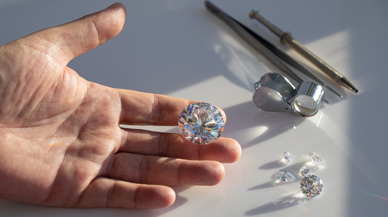 A diamond appraiser holds a diamond as his tools sit on a surface alongside smaller diamonds