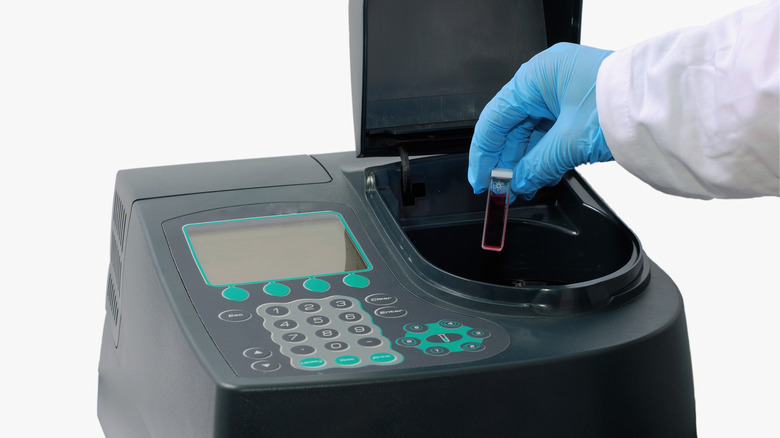 Scientist inserting cuvette with pink liquid into spectrophotometer