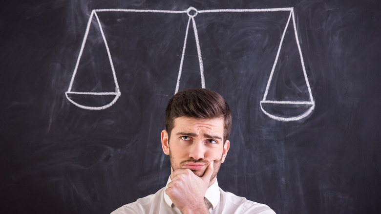 Puzzled man in front of chalkboard with scales drawn on it