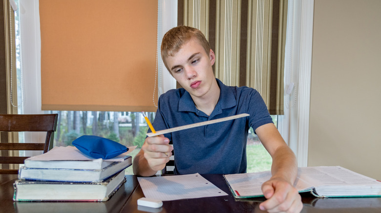 Young man holding ruler at desk with homework