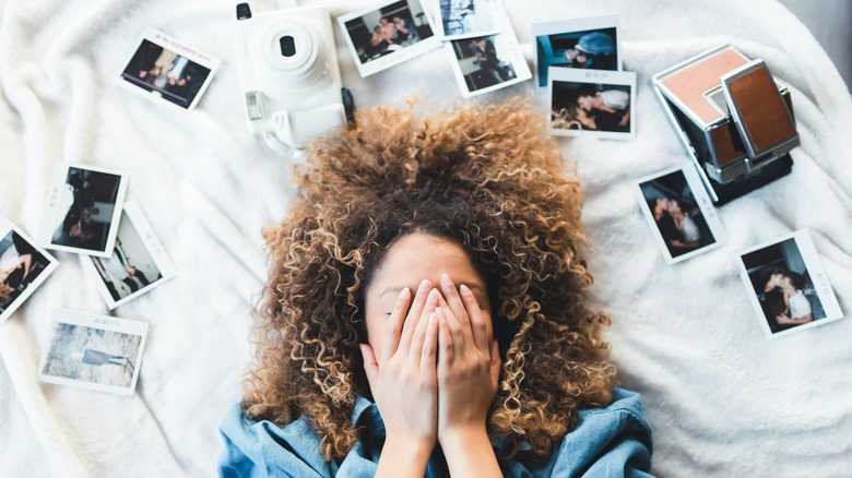 A woman with curly brown hair lying on a bed surrounded by several Polaroid photos