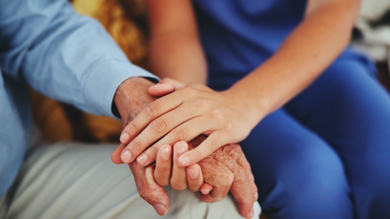 A young woman's hands hold the hand of an older man in close-up