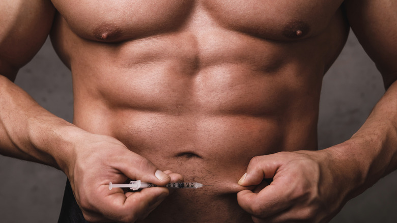 Bodybuilder about to inject abdomen with a syringe