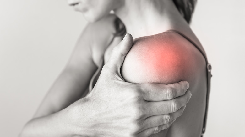 A black and white image of a woman holding her shoulder with red spot indicating pain