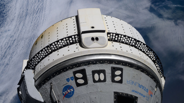 Boeing's Starliner, a hut-shaped capsule, docked at the ISS above clouds in the Earth's atmosphere