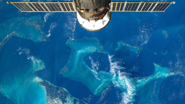 A nodule of the ISS with two solar panel wings stretching out horizontally at the top of the image floats above the blue oceans of the Earth in space