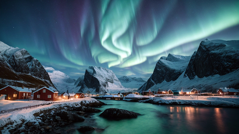 Bands of blue-green light in the sky above a wintery mountain town with towering peaks in the background