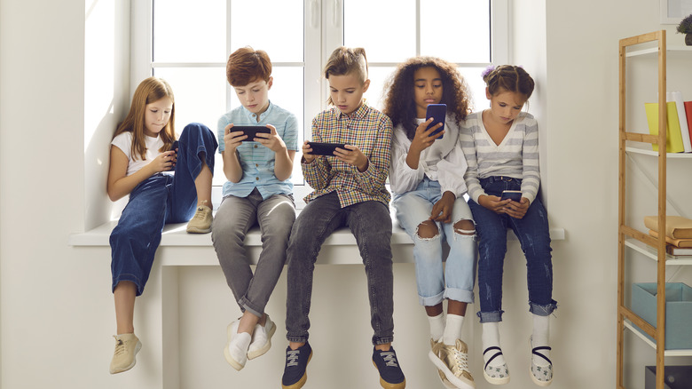 Group of kids on a windowsill staring at their mobile phones