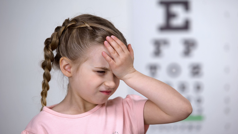 Girl with hand on her head and unfocused Snellen chart in the background