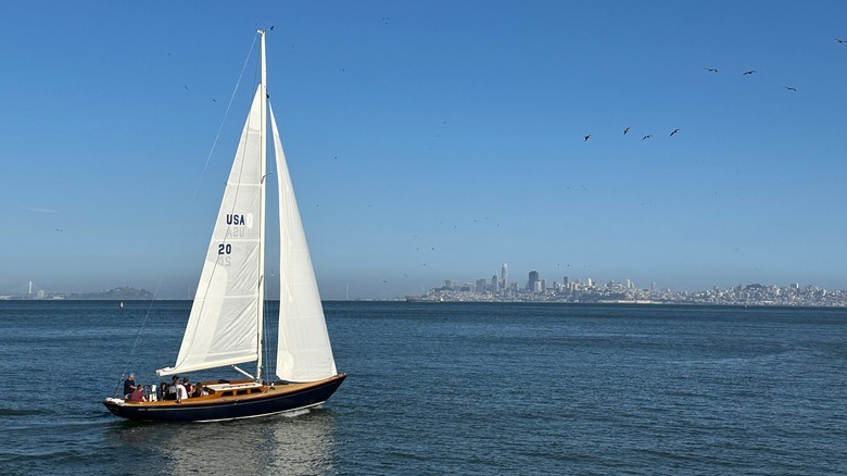 A sailboat is seen on the water below a clear blue sky with a city in the distance