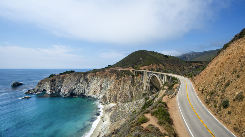 The pacific coast highway passes by a blue bay and cliffs in California