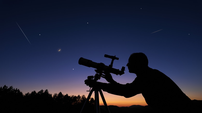 Silhouette of person looking through telescope at night