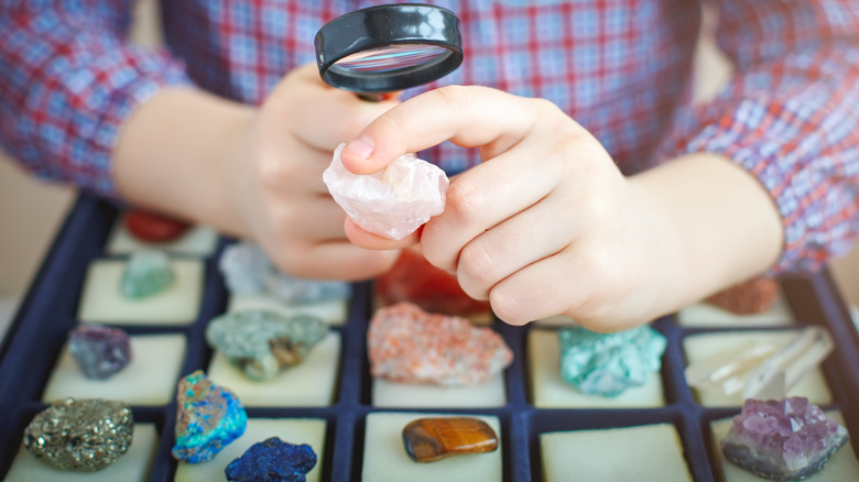 Person looks at a mineral under a magnifying glass with unfocused minerals and gems in the background