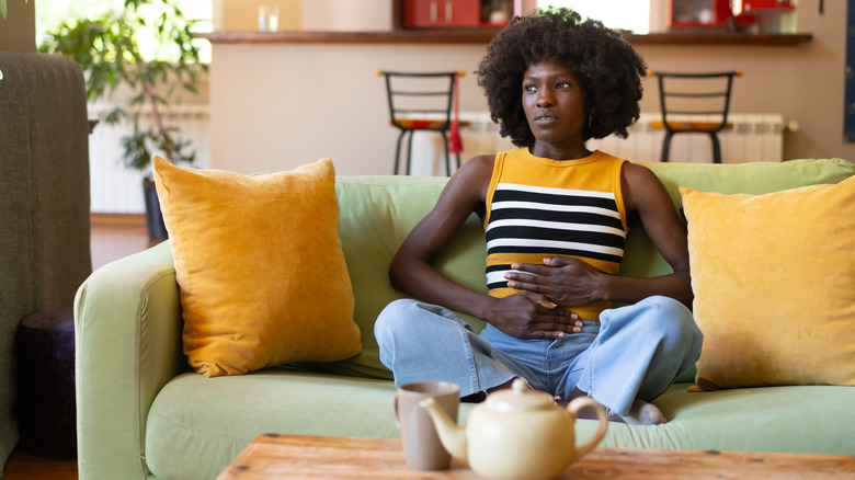 Woman touching her belly and sitting on a green sofa