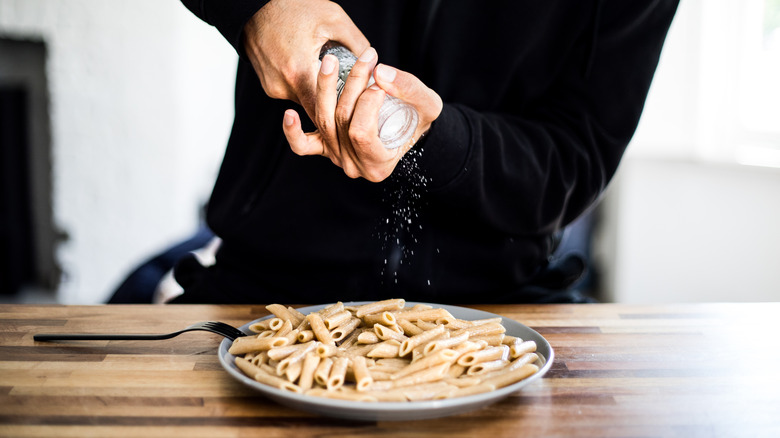 Person adding salt to a plate of pasta