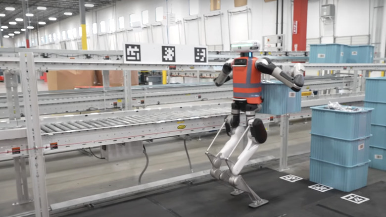 Agility Robotics' Digit robot stands next to a conveyor belt while working in a factory