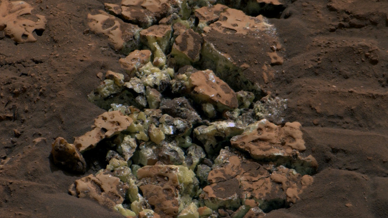 Yellow-green crystals of pure sulfur emerge from reddish rock and sand