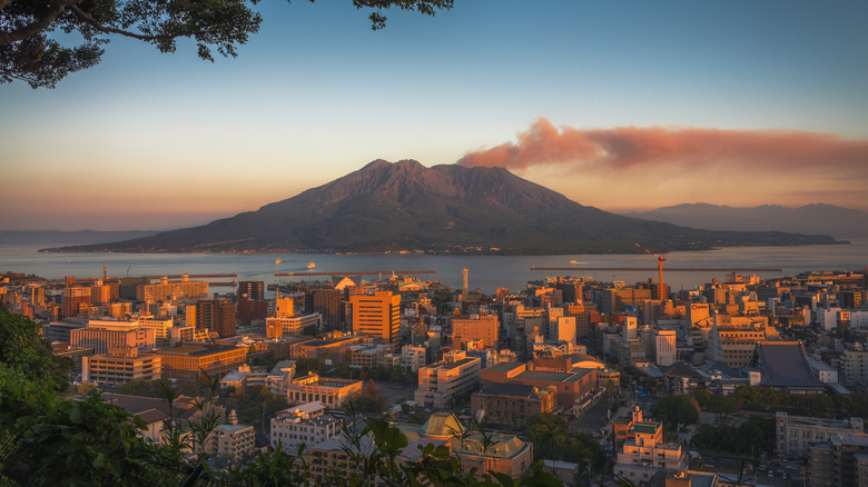 A volcano across a lake with a buildings in sunset light in the foreground