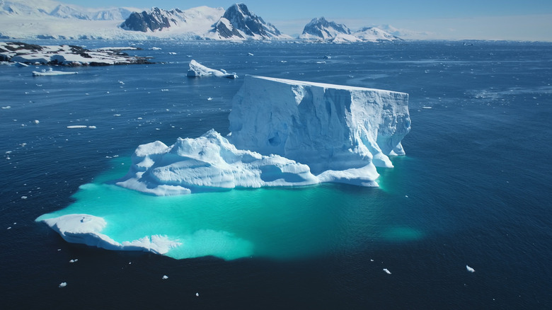 A large iceberg is seen protruding from the ocean with underwater ice clearly visible beneath the water's surface