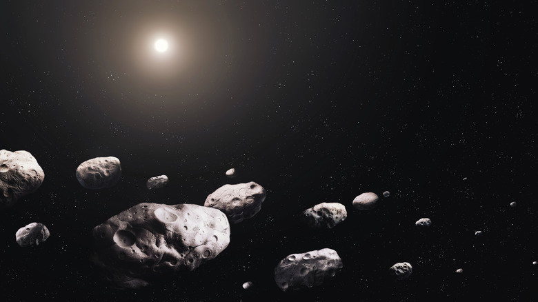 A group of a dozen rocks floating in space with a faint sun in the distance